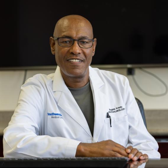 Bogale Aredo, Ph.D., seated at table wearing a white lab coat.