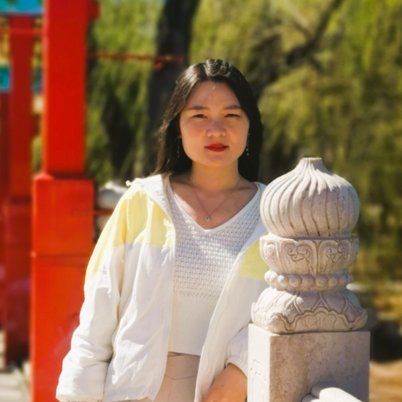 Smiling woman with long dark hair, wearing a white shirt and jacket, standing next to a carved newel post.