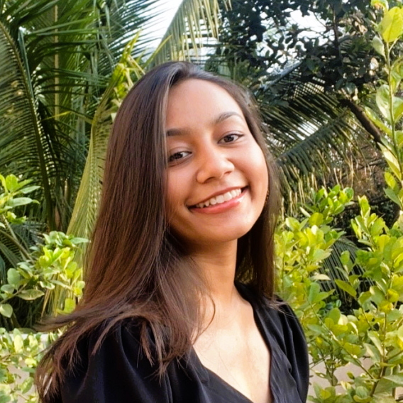Smiling woman with long brown hair, standing next to a fern.