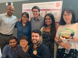 Dr. Malladi and 7 other people pose for the camera in front of poster presentation