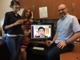 Three team members in lab, with Sean on computer screen