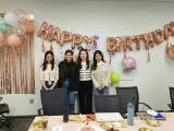 Four women stand in front of a Happy Birthday balloon sign.