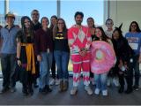 14 lab team members pose in front of a large window, some in costumes.