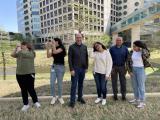 Six people stand outside for a picture; 4 women with long hair struggle with wind blowing their hair while two bald men are unaffected.