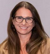 Smiling woman with long dark hear, wearing dark-rimmed glasses.