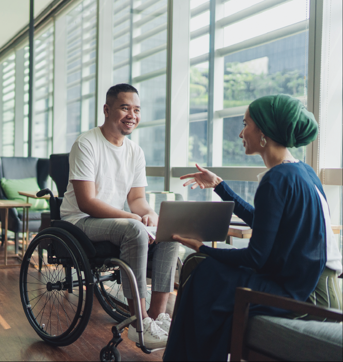 Seated woman holding laptop computer talks with man in wheelchair.