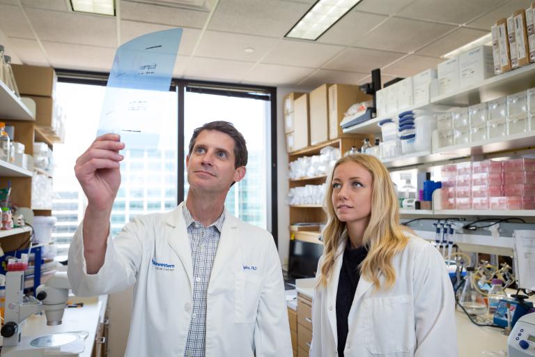 A man and a woman standing in a lab looking at a transparency.
