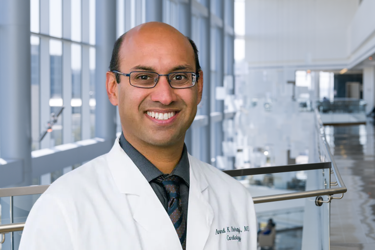 Smiling bald man wearing a lab coat over a dark shirt and tie, and dark-rimmed glasses.