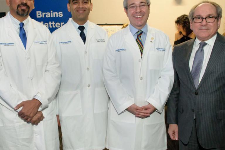 Three doctors wearing white lab coats, stand with man wearing suit.