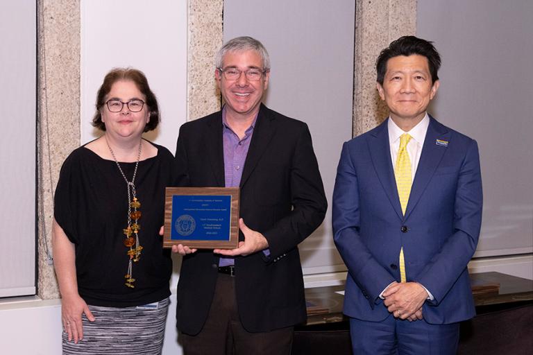 Three professors, with the man in the center holding a placque.