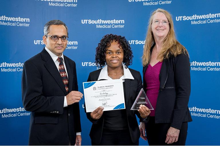 Elviche Lenou accepting an award standing with two administrators standing in front of a blue background