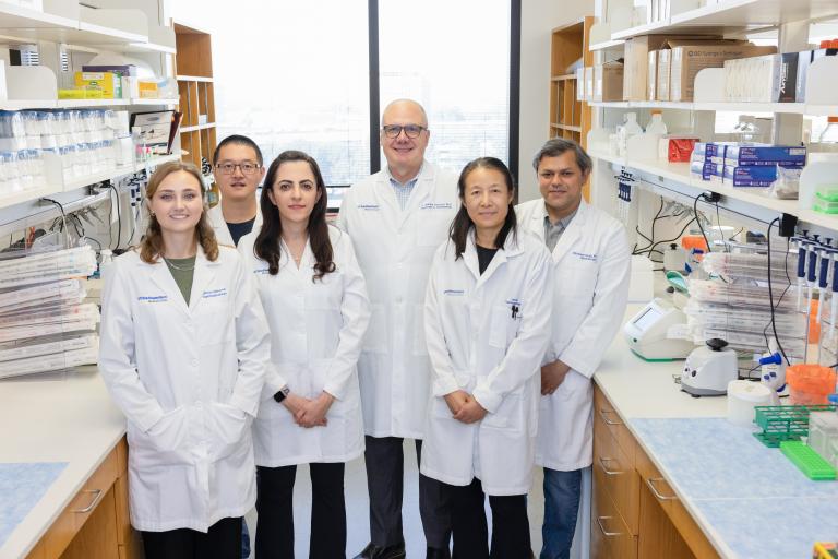 Dr. Harbour and his five lab members wearing white coats standing in his lab.