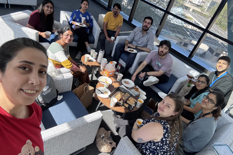 A group of people sitting in a hotel setting with food on a small table in the middle.
