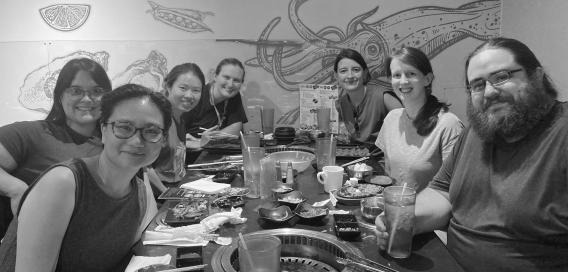 Seven people at a table in a restaurant with a seafood mural behind them.