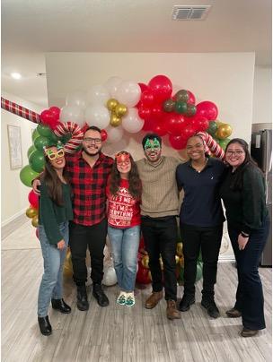 6 masked lab team members with a red, white, green, and gold balloon arch.