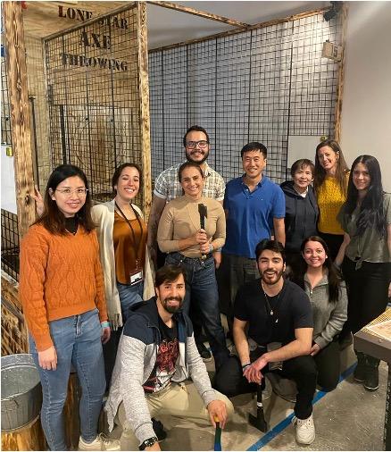 The team pauses for photo outside ax throwing cages, some holding axes.