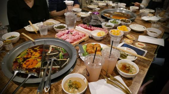 Table spread of various meats, vegetables, and desserts during hot pot lunch. 