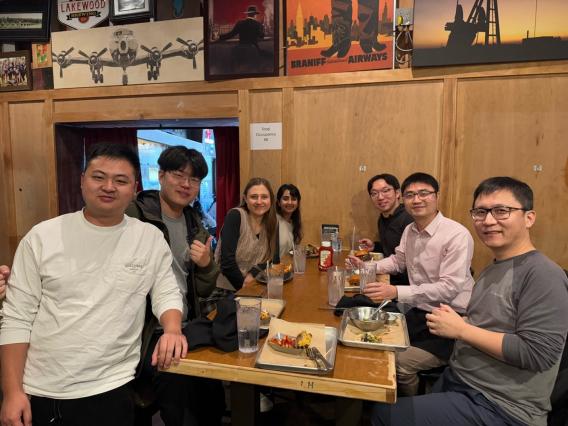 A group of 5 men and 2 women at a restaurant table, smiling.