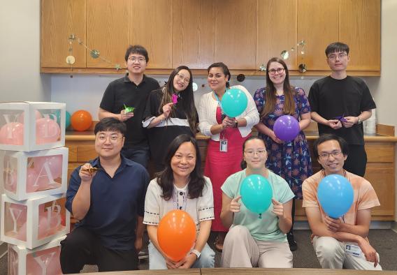 Dr. Dan Tong with eight lab members holding balloons in the lab