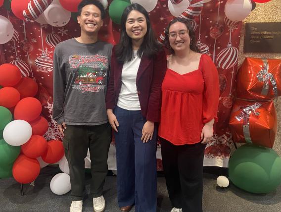 Three people gathered in front of Christmas Decorations.