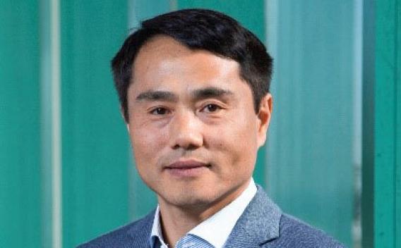 Smiling man with short dark hair wearing a blue jacket over a white shirt.