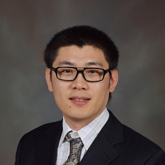 Dark-haired man with glasses wearing dark suit and tie.