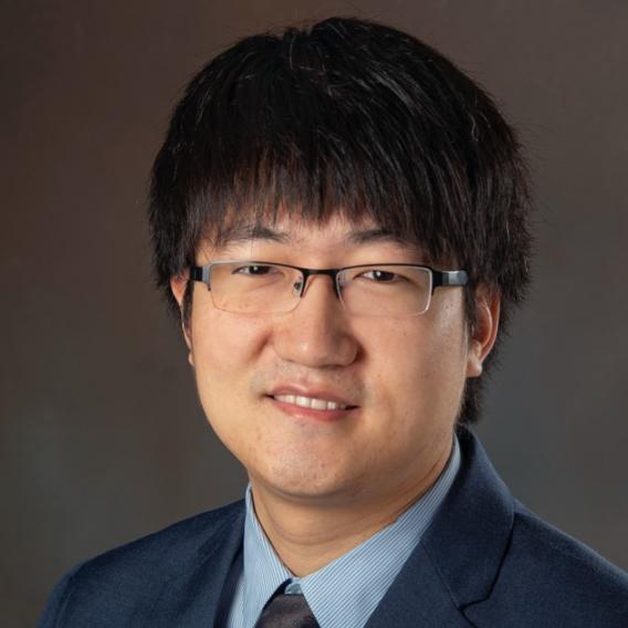 Dark-haired man with glasses wearing dark suit and tie.