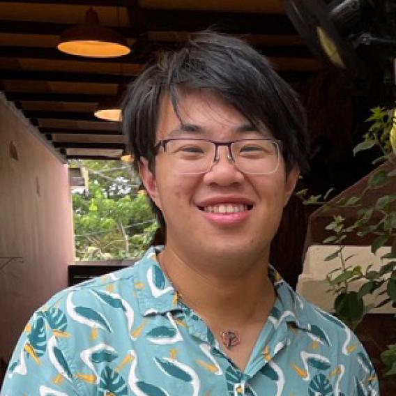 Smiling man with dark hair and glasses, wearing brightly patterned shirt.