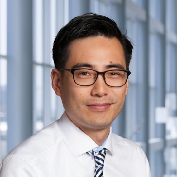 Dark-haired man with glasses wearing lab coat and tie.