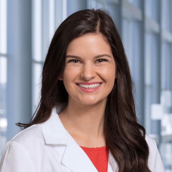 a woman with long dark hair wearing a red shirt under a white coat