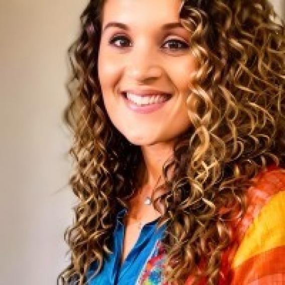 Smiling woman with long brown curls, wearing a brightly colored top.