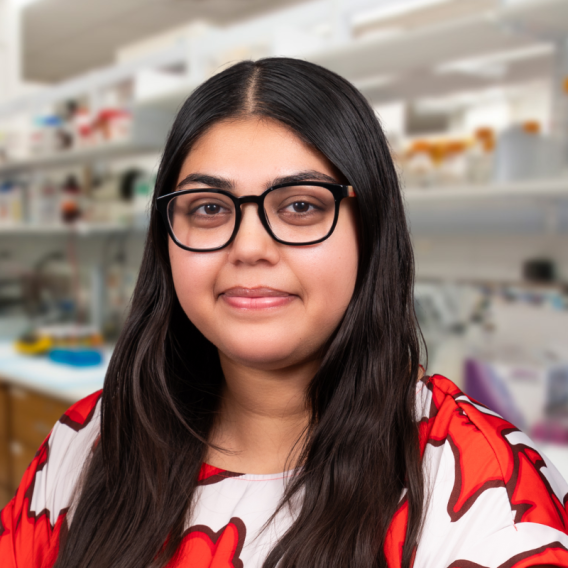 Sneha Banerjee wearing glasses and a red and white shirt standing in a laboratory