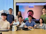 A group of people posed behind a table, in front of a large screen.