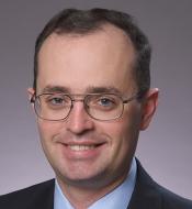 Smiling man with thin brown hair and wire rimmed glasses.