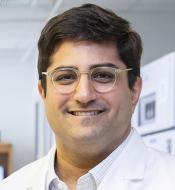 Smiling man with thick dark hair, wearing glasses with clear plastic frames.