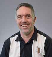 Grinning man with gray hair, wearing a black and white shirt.