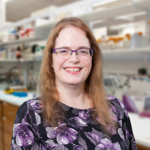 a woman with red hair wearing a floral shirt standingin a laboratory