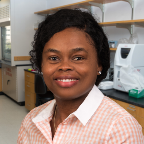 a woman with dark hair wearing a pastel checkered shirt standing in a research laboratory.