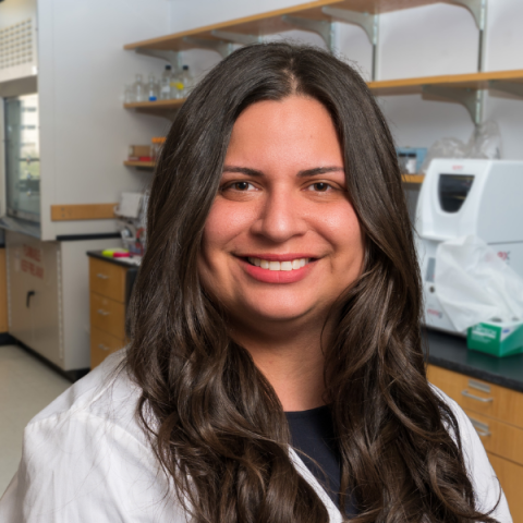 Laura Hansen wearing a white lab coat and standing in a laboratory