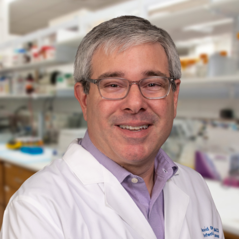 Dr. David Greenberg in a white coat standing in a laboratory