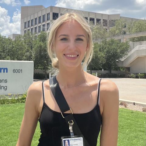 Smiling blond woman in a black tank top, standing outside in front of UTSW.