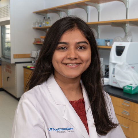 a woman with long dark hair wearing a white lab coat standing in research laboratory.