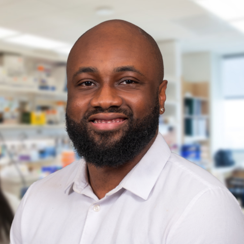 a man with a beard, wearing a white shirt standing in a research lab