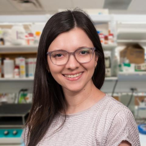 a woman with long brown hair wearing glasses standing in a research lab