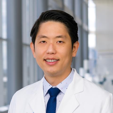 a man with short dark hair wearing a white lab coat an