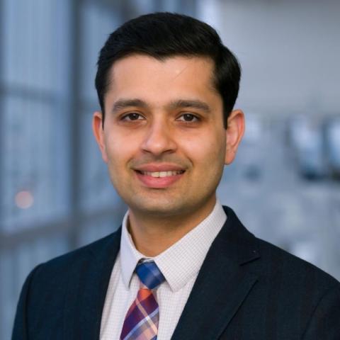 headshot of Dr. Kartavya Sharma, dark haired man in dk blue suit, white shirt, and plaid tie