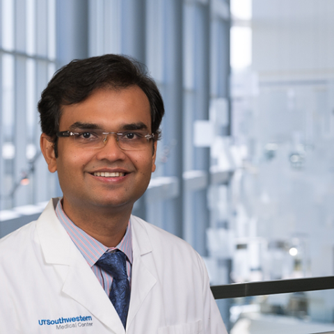 Dr. Ambarish Pandey wearing glasses, a white lab coat and striped shirt standing in the Clements University Hospital lobby